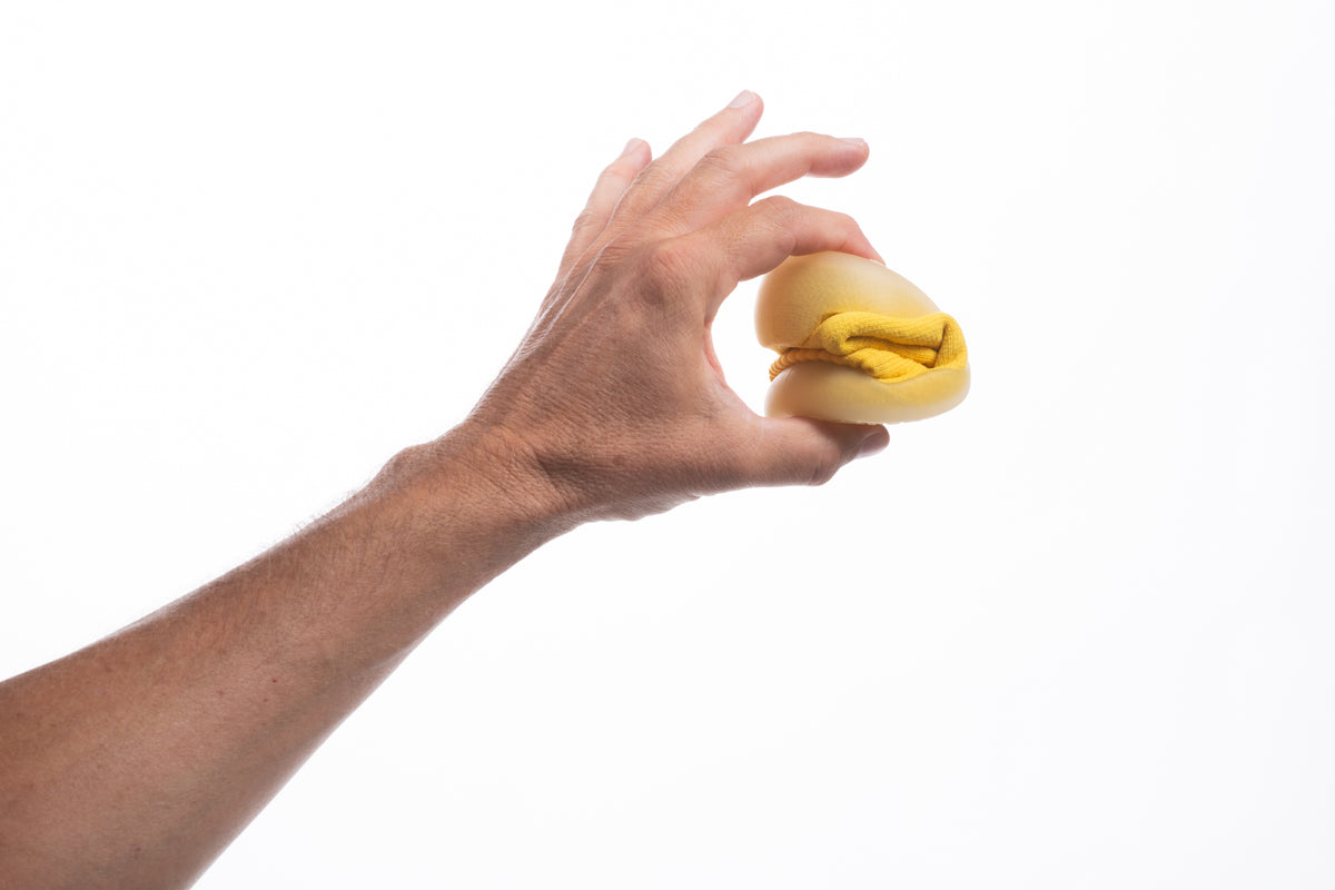 A hand squeezing a yellow sock shoe flat to show how thin and flexible the sole is