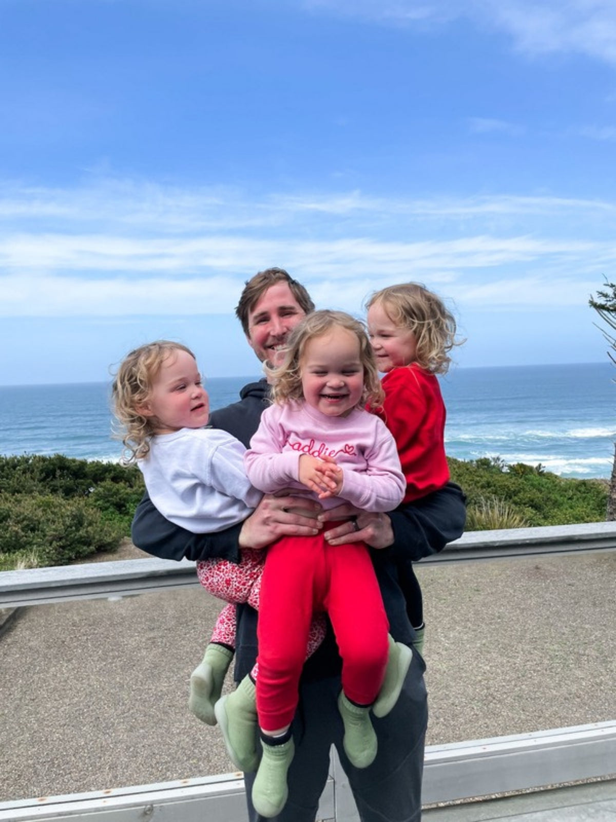 Tyler holding his triplet daughters on the Oregon coast